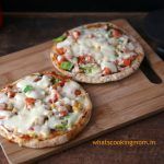 two small pizzas sitting on top of a wooden cutting board