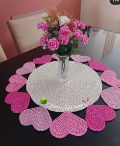 a vase filled with pink flowers sitting on top of a table covered in crochet hearts