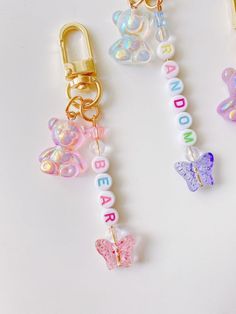 three keychains with letters and butterflies attached to them, on a white surface