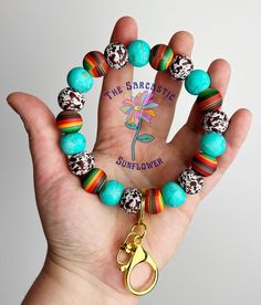 a hand holding a bracelet with colorful beads and a gold charm that says the sarcastic sunflower