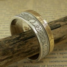 Sterling Silver and 10K Yellow Gold with Claddagh and Celtic Knot Design around the entire ring. A custom personalized phrase in Ogham on 10K yellow rail edge. Claddagh & Celtic Knot Wedding Band with Ogham Script Rail. Handmade in Ireland. 7.5 mm wide. Available in whole & half Sizes 4.5 to 13. Florentine background with polished design, your personalized phrase in Ogham Script on rail edge. Comfort Fit. Irish Hallmark. The phrase is usually a name or word or short phrase. Start a conve Unique Engraved Wedding Ring With Etched Design, Unique Engraved Ring For Wedding, Unique Engraved Etched Wedding Ring, Ceremonial Silver Engraved Ring Stamped 14k, Ceremonial Silver Engraved Ring, Stamped 14k, Traditional Jewelry With Engraving Option For Anniversary, Symbolic Engraved Wedding Ring With Engraving Option, Engraved White Gold Jewelry For Marriage, Unique Engraved 14k Gold Ring For Wedding