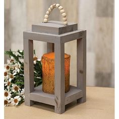 a small wooden lantern with a beaded handle on it and flowers in the background