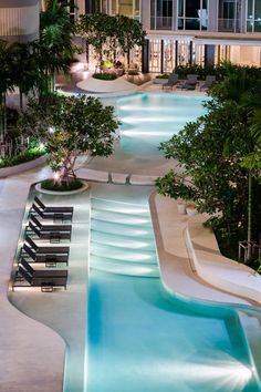 an empty swimming pool at night with lounge chairs and trees in the foreground, surrounded by apartment buildings