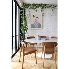 a dining room with white brick walls, wooden chairs and an art work on the wall