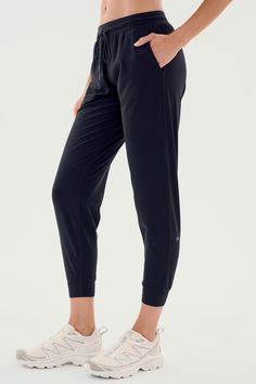 A person is shown wearing SPLITS59's Classic Airweight Jogger in Black and white athletic shoes. The focus is on the side view of the lower body, perfect for a workout. Sporty Activewear With Functional Drawstring Long Pants, Athleisure Joggers With 4-way Stretch And Elastic Side Panels, Stretch Activewear For Jogging With Functional Drawstring, Sporty Joggers With Functional Drawstring, Athleisure Joggers With Stretch And Functional Drawstring, Stretch Athleisure Joggers With Functional Drawstring, Solid Activewear With Elastic Waistband For Jogging, Athleisure Activewear With Comfort Stretch, Athleisure Activewear With Comfort Stretch And Elastic Side Panels