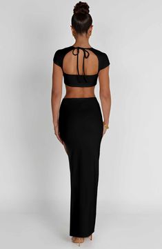 the back of a woman wearing a black crop top and long skirt with cut outs