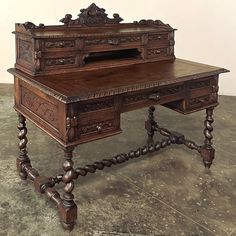 an old wooden desk with ornate carvings on the top and bottom drawers, sitting on concrete flooring