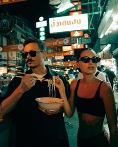 a man and woman eating noodles in the middle of a busy city street at night