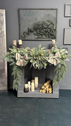 a mantle with candles and greenery on it in front of a wall hanging art piece