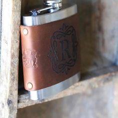 a brown leather flask with the initials r and f on it, hanging from a wooden shelf