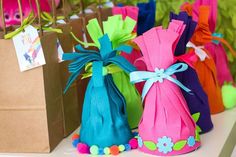 colorful bags with pom poms are lined up on a table in front of small brown paper bags