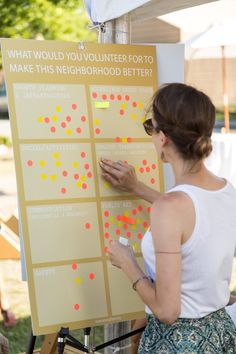 a woman standing next to a sign with dots on it and writing on the board