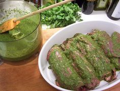 a bowl filled with meat covered in pesto next to bottles of wine and vegetables