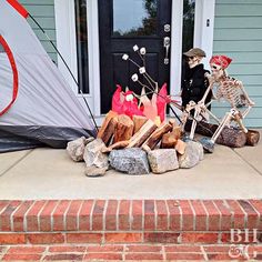 a skeleton sitting on the front porch next to a tent and firewood with bags