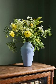 a blue vase filled with yellow flowers sitting on top of a wooden table next to a book shelf