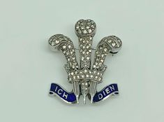 A gorgeous vintage art deco rhodium finished sterling silver brooch in rare prince of wales feathers design. Decorated with blue enamel ICH DIEN banner and set with round cut paste which are meant to simulate diamonds. A rare piece by quality maker Ciro. Maker/Markings: Marked SCP for Silver Ciro Pearls Condition: Very Good Used Condition - Please look at photos Measurements: 1 1/8" x 7/8" wide ~ 28 x 23mm Weight: 6.4g Prince Of Wales Brooch, Collectible Hallmarked Blue Brooches, Antique White Gold Collectible Brooches, Silver Elegant Enamel Pin For Formal Use, Silver Elegant Enamel Pin For Formal Events, Elegant Silver Enamel Pin For Formal Occasions, Formal Silver Enamel Brooches, Art Deco Engraved Brooch For Formal Occasions, Art Deco Engraved Brooches For Formal Occasions