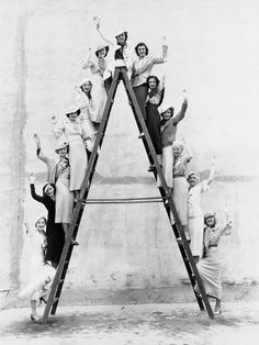 vintage black and white photo of people on a ladder posing for the camera with their hands in the air