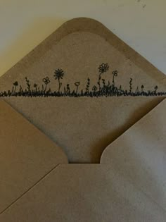 an envelope with a drawing of flowers and grass on the inside is open to reveal a piece of brown paper