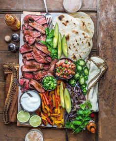 an assortment of meats and vegetables on a plate with pita bread, avocado, salsa, lime wedges