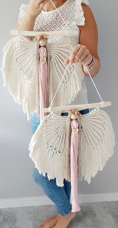 a woman is holding two pieces of white crochet with pink tassels