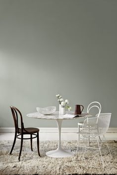 two chairs and a table in front of a gray wall with white flowers on it