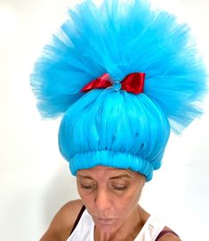 a woman with bright blue hair and a red bow on her head is looking down