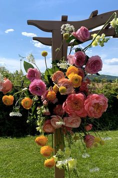 a bunch of flowers that are sitting in the grass near a wooden structure with a cross on it