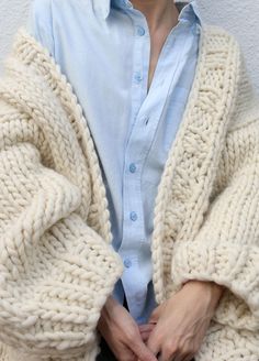 a woman wearing a blue shirt and white cardigan sweater with her hands in her pockets