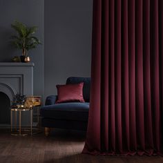 a living room with a blue couch, red curtains and a fire place in the corner