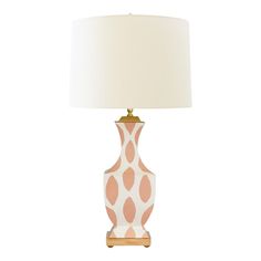 a pink and white lamp with a beige shade on it's base, sitting next to a white wall