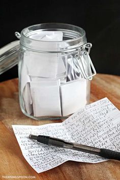 a glass jar filled with notes and a pen on top of a wooden table next to it