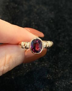 a woman's hand holding a ring with a red stone