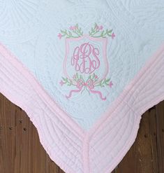 a pink and white quilted blanket with an embroidered monogrammed initials on it