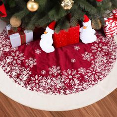 a christmas tree skirt with snowmen and presents under it on a table top next to a small christmas tree