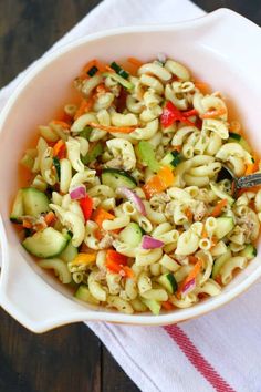 a white bowl filled with pasta and veggies next to some carrots on a towel