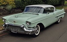 an old green car is parked on the side of the road in front of some bushes