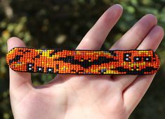 a hand holding an orange and black beaded object