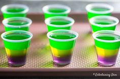 there are many glasses with different colored liquids in them on the tray and one is empty