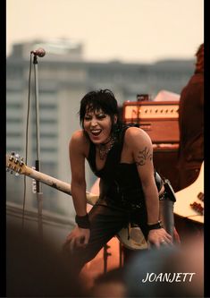 a woman holding a guitar on top of a roof next to a microphone and amp