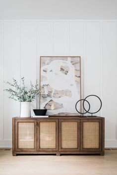 an art piece on top of a wooden cabinet in front of a painting and plant