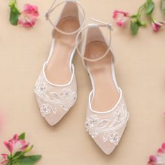 a pair of white shoes sitting on top of a table next to some pink flowers