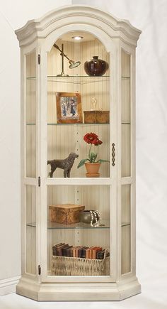 a white china cabinet with glass doors and shelves filled with vases, flowers and pictures