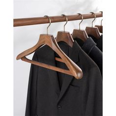 wooden clothes hangers are hanging on a white wall and two black suits in the background