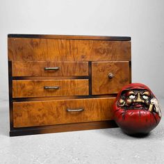 a wooden dresser sitting next to a red and black vase on top of a white floor