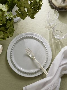 an empty plate on a table with silverware and napkins next to some plants