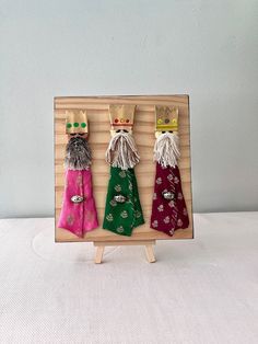 three napkins with crowns on them are in a wooden frame, one is red and the other is green