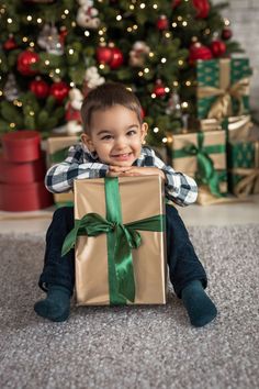 a young boy sitting in front of a christmas tree holding a present