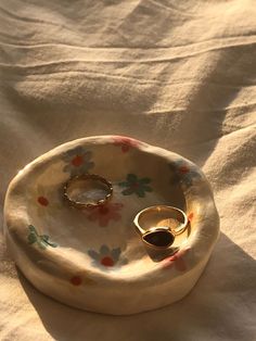 two gold wedding rings sitting on top of a flowered plate with an oval ring holder