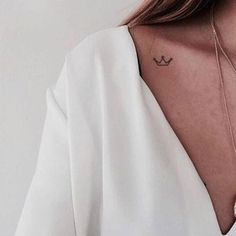 a woman wearing a white shirt has a small anchor tattoo on her chest