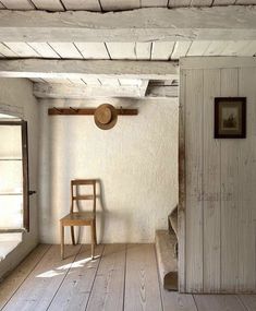 an empty room with a chair, window and wooden door in the corner that leads to another room